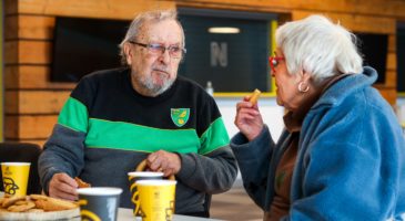 Two older people chat over tea and biscuits