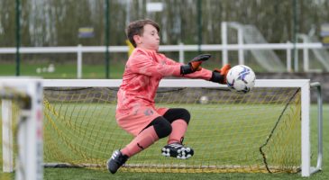 Goalkeeper wearing orange kit saves a shot