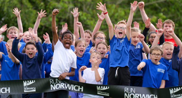 children raising their arms behind a Run Norwich banner