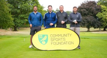 Four golfers standing behind a community Sports Foundation banner