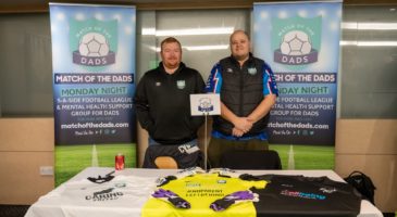 two men standing in front of charity posters