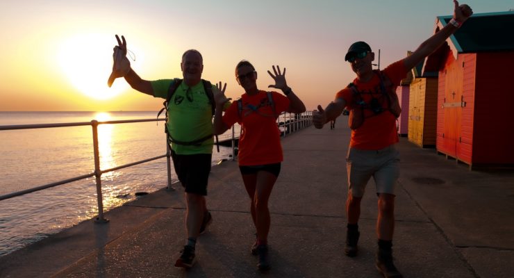 three people walking along the coast with the sunrise behind them