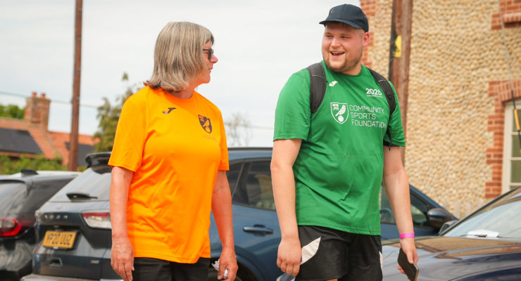 women in orange top and man in green top walking alongside each other