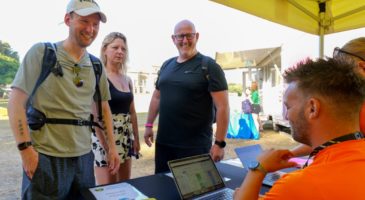 three people standing in front of a man sitting with a laptop