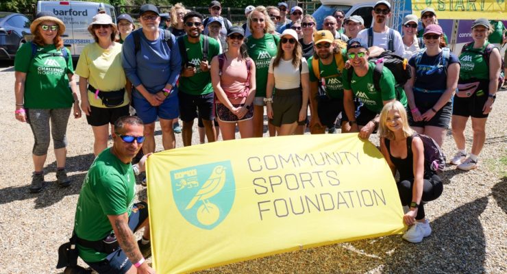 group of people standing around a community sports foundation flag