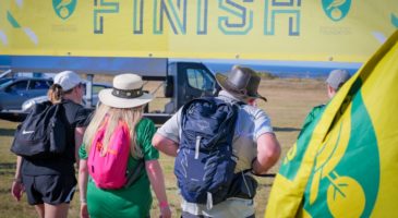 two people with rucksacks walking underneath finish banner