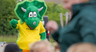dinosaur mascot wearing a yellow top