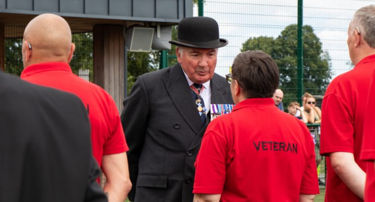 man in bowler hat talking to person with red top