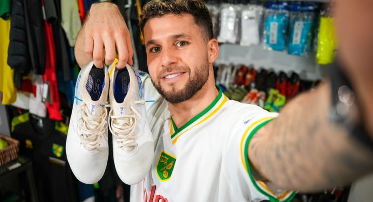 man in white top holding a pair of football boots