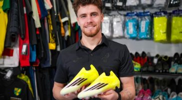 man in black top holding a pair of football boots