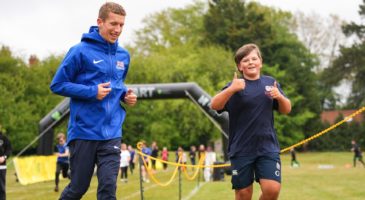 man in blue top running next to a boy with his thumbs up