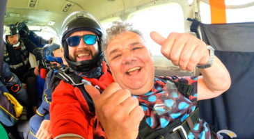 two men sitting in a plane, one giving a thumbs up