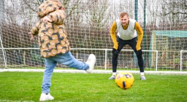 a young boy kicking a ball at a norwich city player