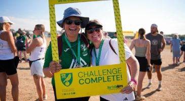 two women posing behind a challenge complete sign