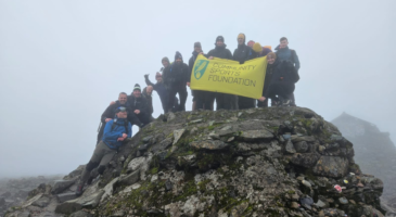 Group on people on the summit of Ben Nevis holding a community sports foundation banner
